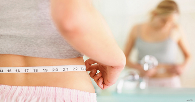 A woman measures her waist as she prepares for a mommy makeover. 